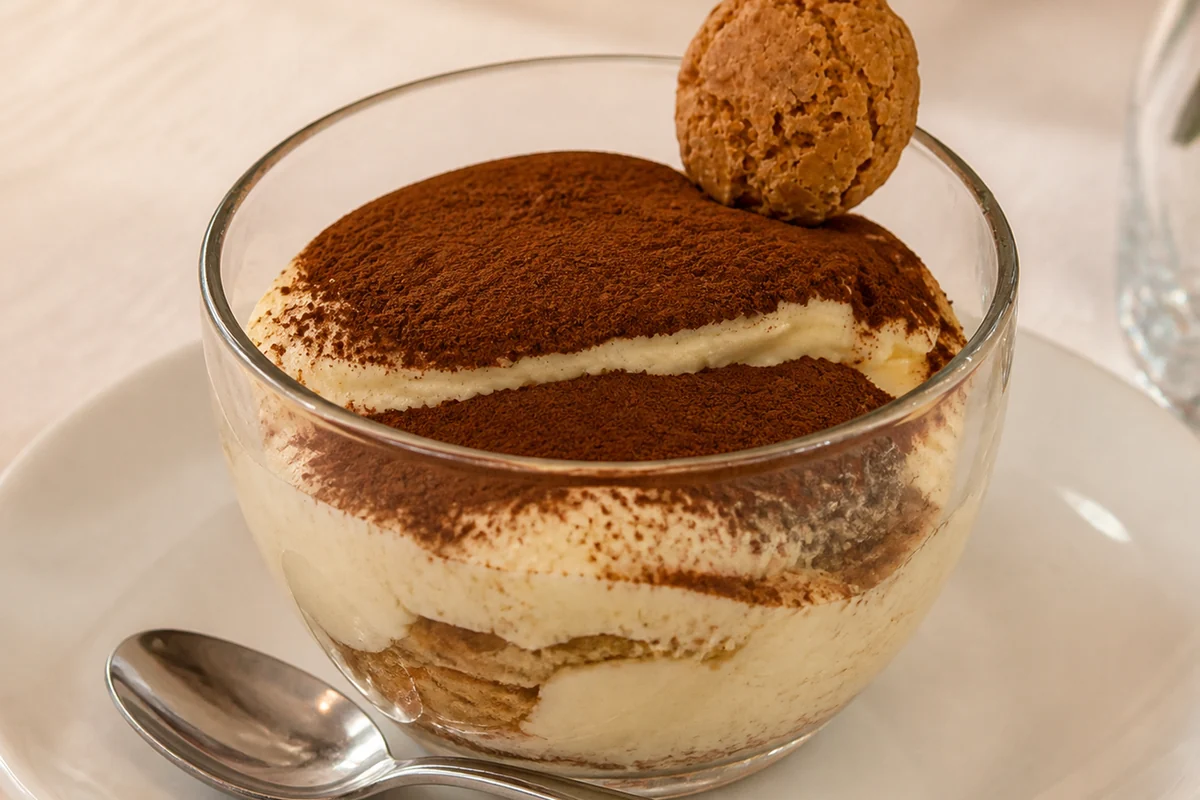 House tiramisu served in a glass with cocoa and an amaretti biscuit